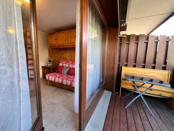 Una habitació amb un llit de fusta, una taula petita i una finestra amb vista a una tanca de fusta.