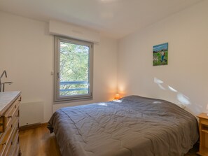 Une chambre à coucher avec un lit, une fenêtre, une table de chevet avec une lampe et un tableau accroché au mur.