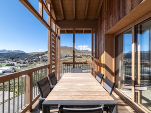 A wooden deck with a long table and chairs, overlooking a mountainous landscape. - Résidence Phoenix — Espace bien-être & salle de sport au cœur de la montagne (Huez)