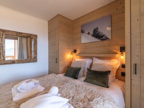 A bedroom with a bed, pillows, a mirror, and a painting on the wall. - Résidence Phoenix — Espace bien-être & salle de sport au cœur de la montagne (Huez)