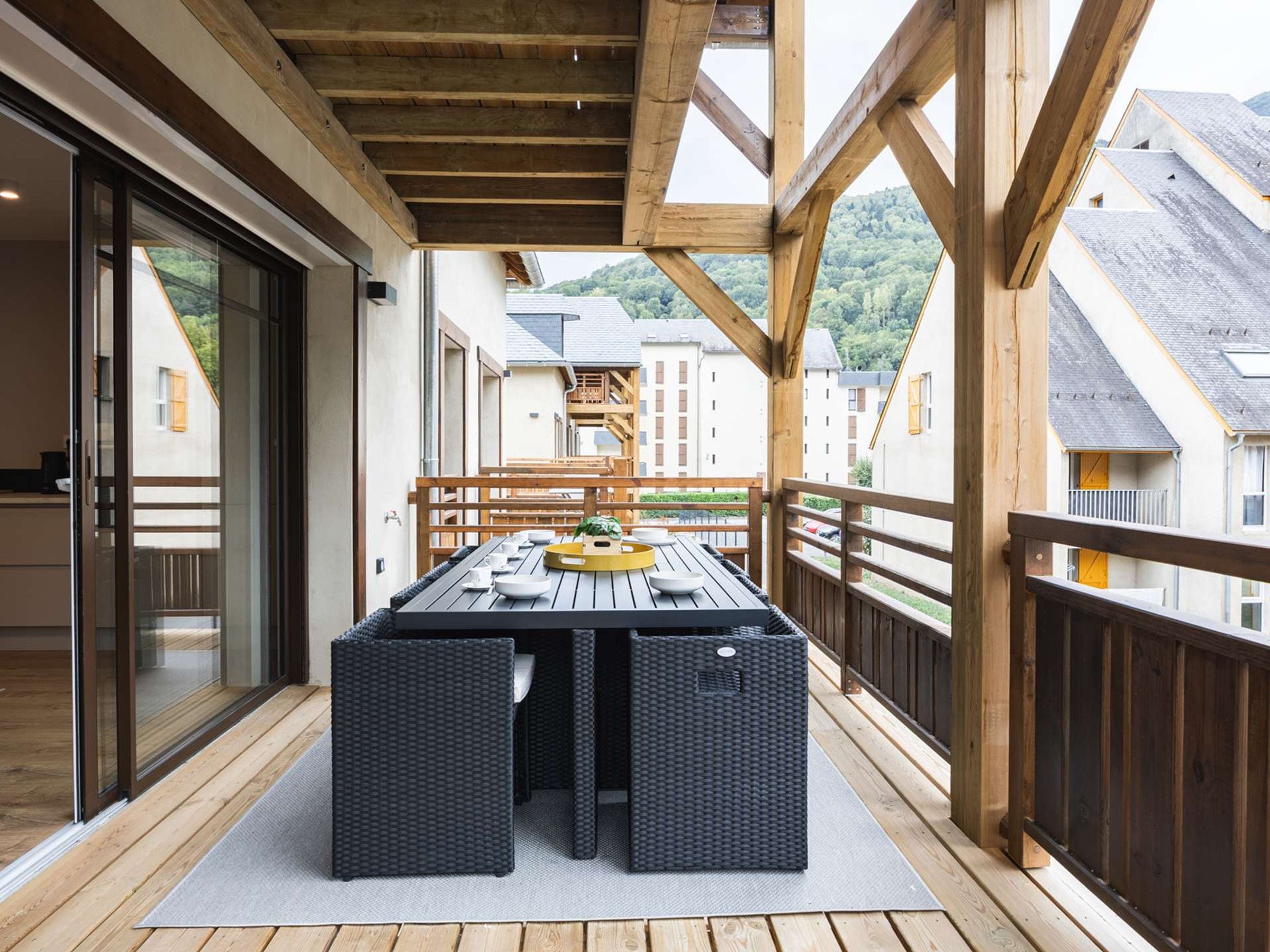 Un espace de restauration en plein air avec une table dressée pour quatre personnes, entouré de rampes en bois et donnant sur un quartier résidentiel.