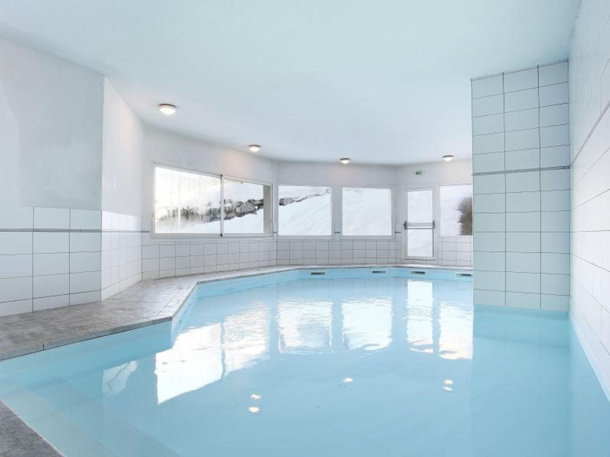 An indoor swimming pool with tiled walls and windows.