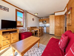 A cozy living room with a TV, red sofa, wooden coffee table, and a dining area with a table and chairs. - Cosy apartment, pets allowed - 4 guests, mountain view (Notre-Dame-de-Bellecombe)