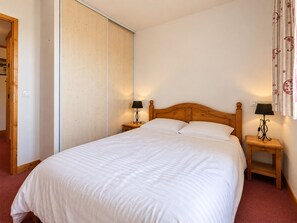 Een slaapkamer met een groot bed, een houten hoofdbord, twee nachtkastjes met lampen en een schuifdeurkast.