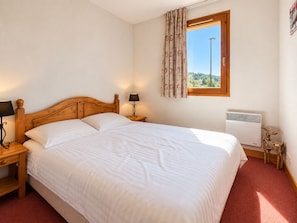 A bedroom with a wooden bed, a nightstand with a lamp, a window with curtains, and a radiator. - Cosy apartment, pets allowed - 4 guests, mountain view (Notre-Dame-de-Bellecombe)