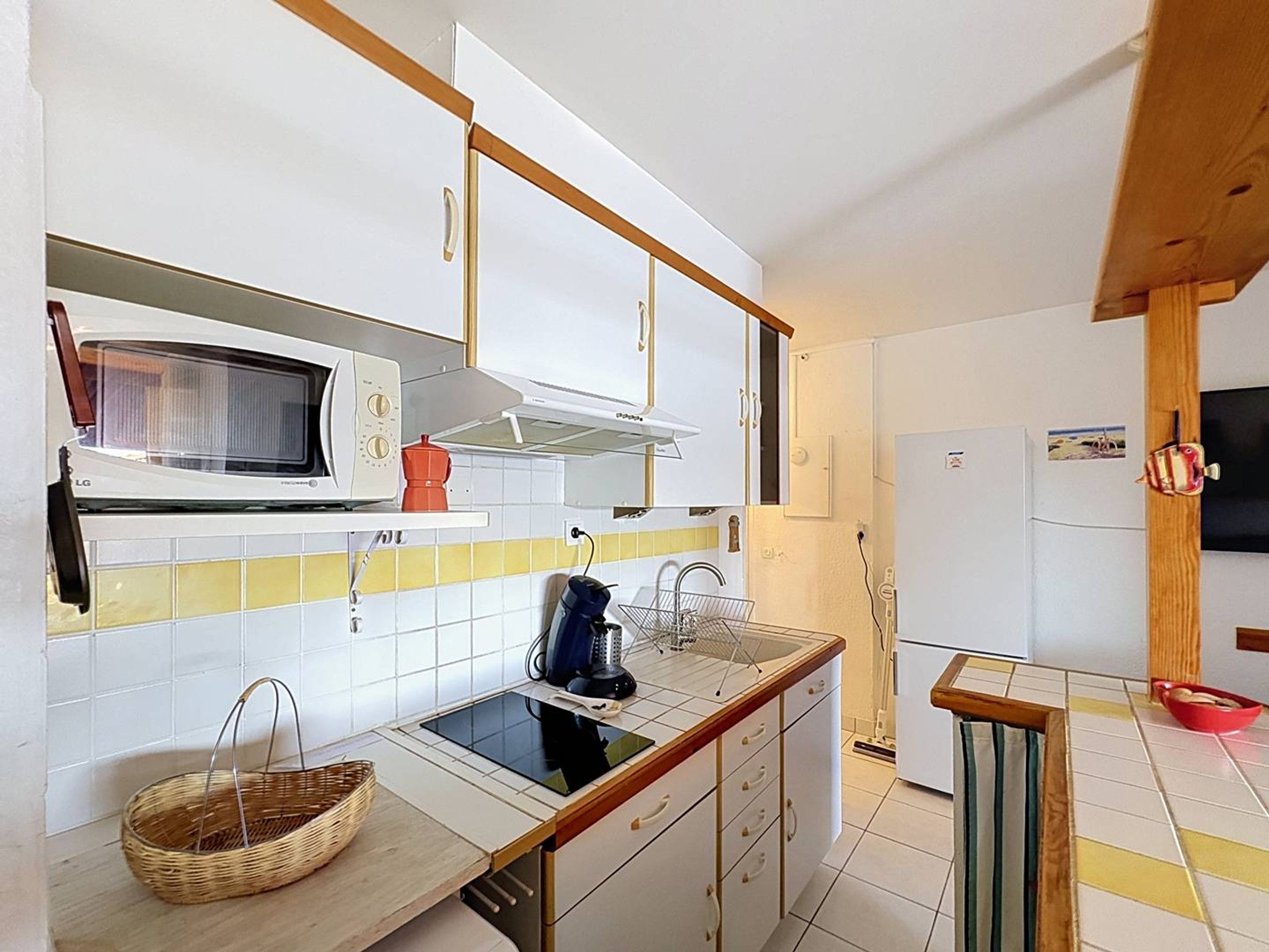 A kitchen with white cabinets, a microwave, a kettle, and a sink.