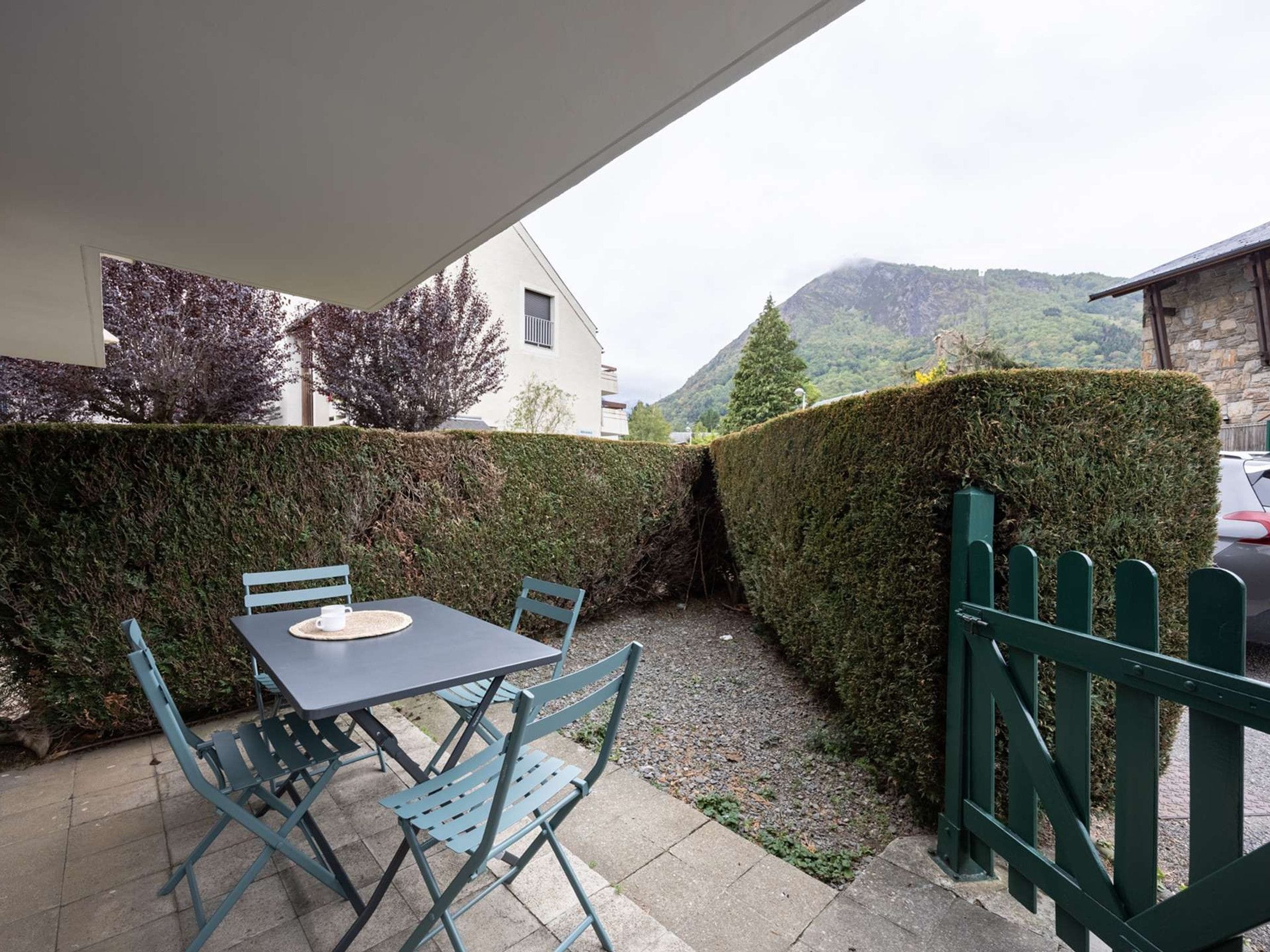 Un patio con una mesa y sillas, una valla verde y vistas a la montaña.