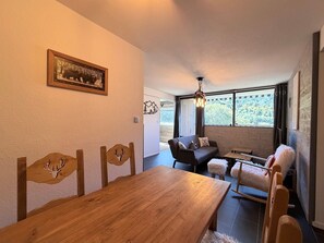 A dining area with a wooden table and chairs, a sofa, and a small table with a lamp. - Apartment with nature view - 4 guests (Mont-Dore)