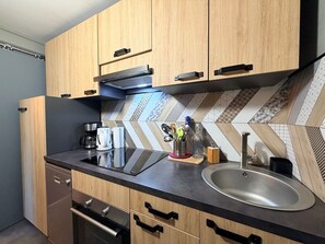 Eine moderne Küche mit Holzschränken, einer schwarzen Arbeitsplatte, einer Edelstahl-Spüle und einer strukturierten Spritzschutzwand.