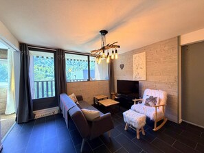 A modern living room with a sofa, a wooden rocking chair, a television, and a fireplace. - Apartment with nature view - 4 guests (Mont-Dore)