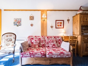 A cozy living room with a patterned sofa, wooden furniture, and wall decorations. - Studio · Ski aux pieds · Balcon (Bourg-Saint-Maurice)