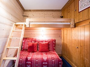 En våningssäng med en stege, träväggar och ett rött, mönstrat överkast.