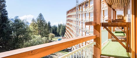 A wooden balcony with a view of a forested area and a building with multiple balconies.