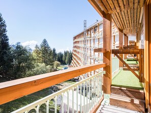 A wooden balcony with a view of a forested area and a building with multiple balconies. - Studio · Ski aux pieds · Balcon (Bourg-Saint-Maurice)
