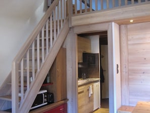 A wooden staircase leading to a kitchen area with a microwave, toaster, and cabinets. - Studio apartment at the foot of the slopes - 6 guests (Huez)
