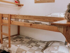 A bunk bed with a wooden frame, a lower bunk with patterned bedding, and a shelf above the bed. - Studio apartment at the foot of the slopes - 6 guests (Huez)