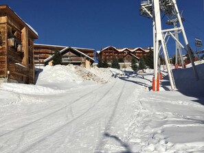 A snow-covered road leading to a lodge with wooden architecture and a ski lift in the background. - Studio apartment at the foot of the slopes - 6 guests (Huez)