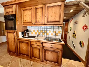 A kitchen with wooden cabinets, a black stove, a tiled backsplash, and a refrigerator with stickers. - Spacious apartment at the foot of the slopes - 6 guests (Morillon)