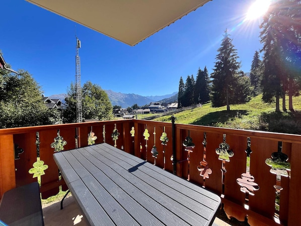 A wooden deck with a table and chairs, overlooking a mountainous landscape with trees and a clear sky. - Spacious apartment at the foot of the slopes - 6 guests (Morillon)