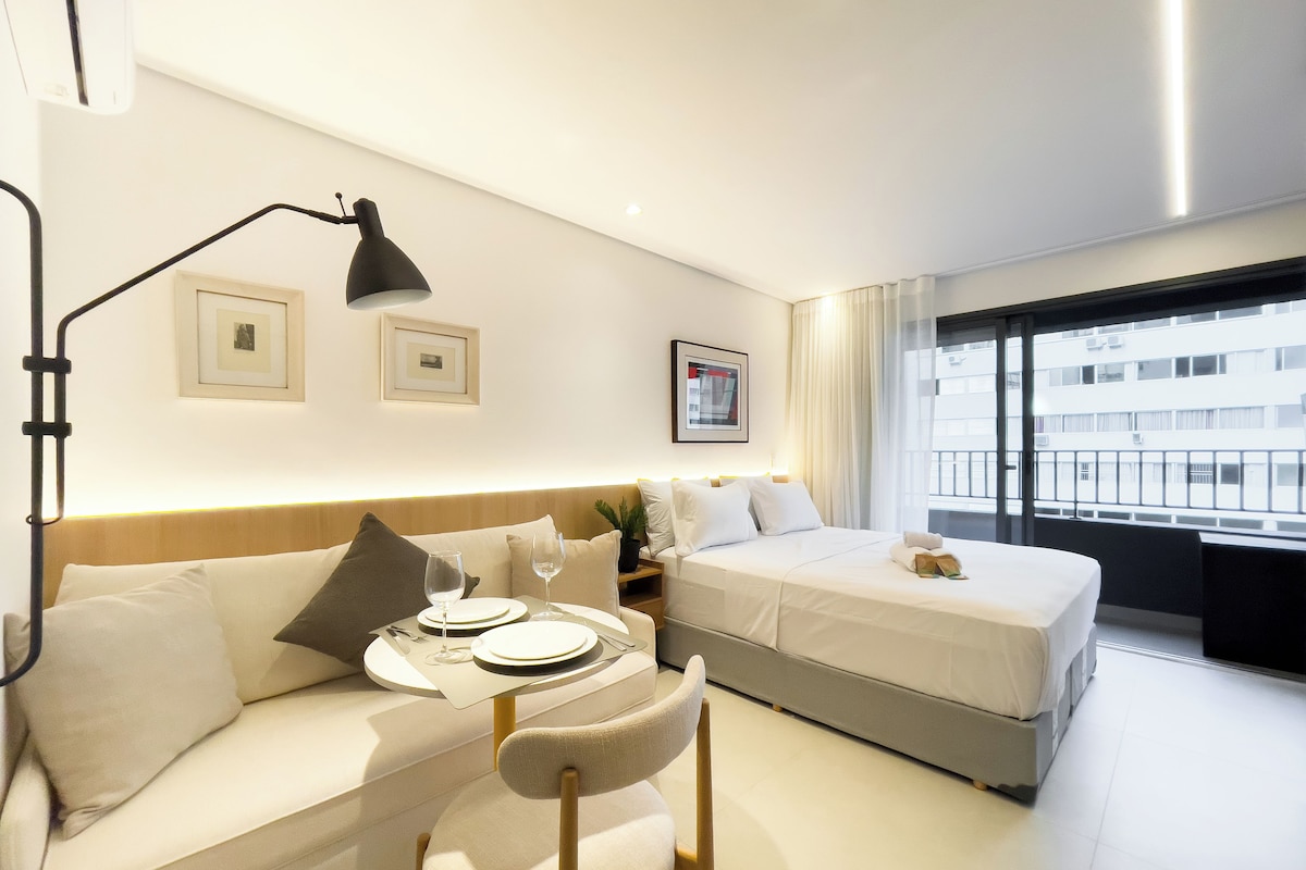 Una camera d'albergo con un divano, un letto, un tavolo da pranzo con piatti e bicchieri, e una finestra vista edifici.