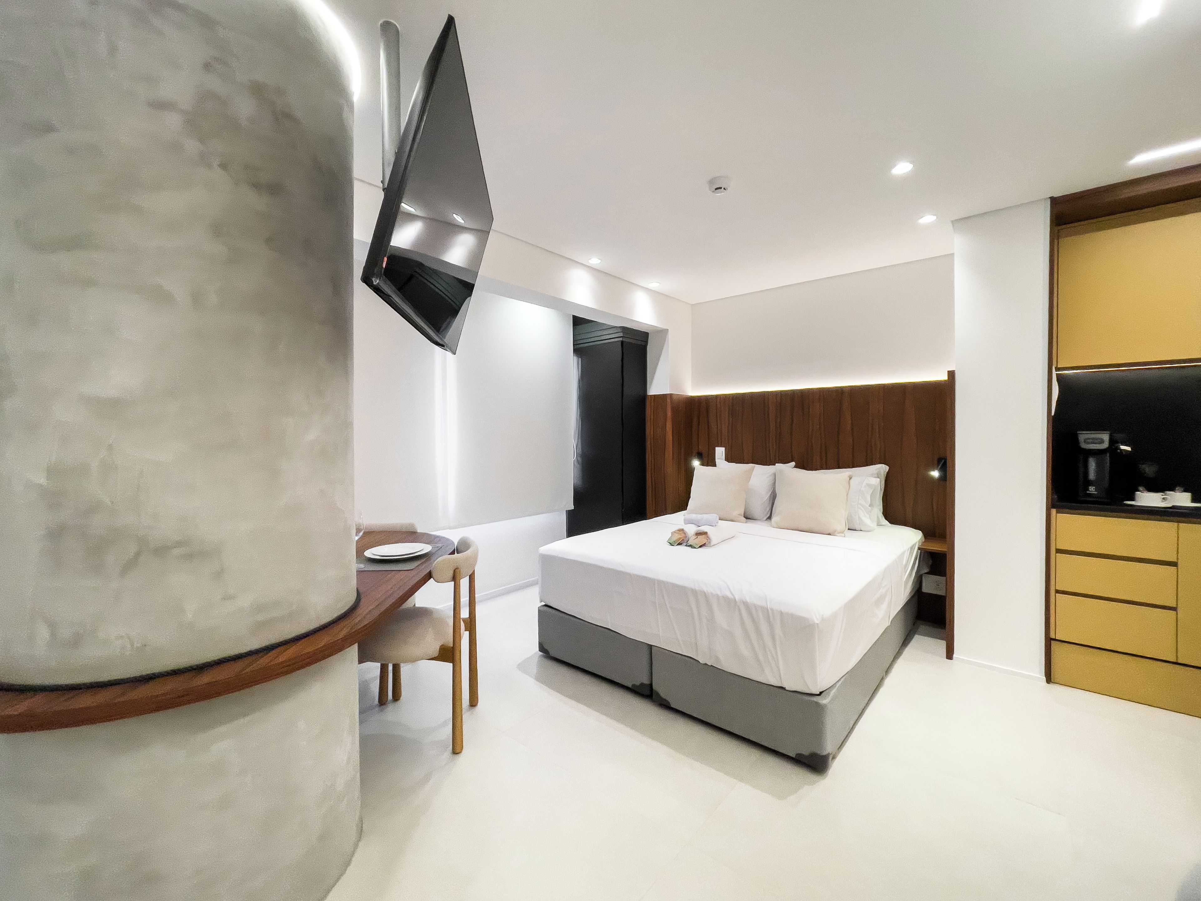 Quarto de hotel moderno com cama, mesa de cabeceira e televisão de tela plana na parede.