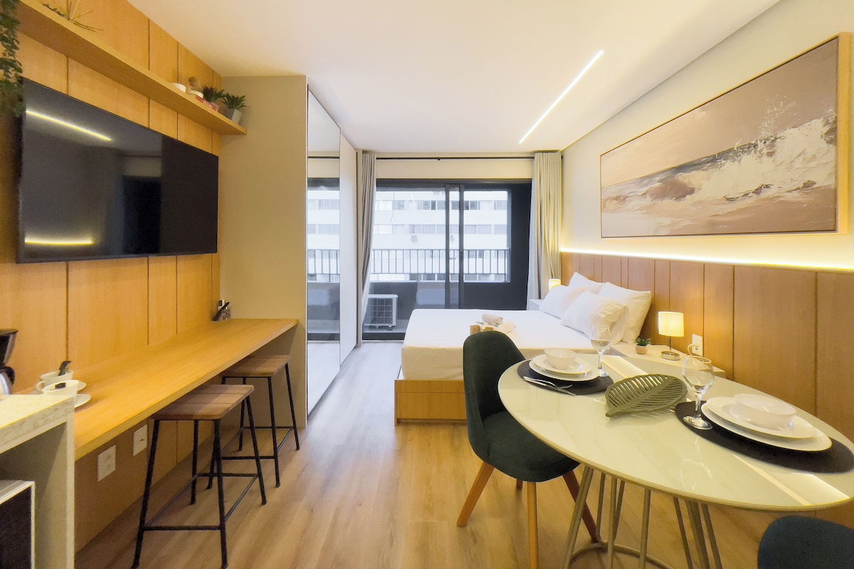 Una camera d'hotel con un letto, un tavolo da pranzo con sedie, una TV a parete e una finestra vista sulla città.