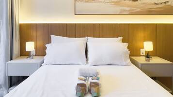A neatly made bed with white linens, two pillows, and a pair of folded towels. There are two bedside lamps on either side of the bed, and a painting above the headboard.
