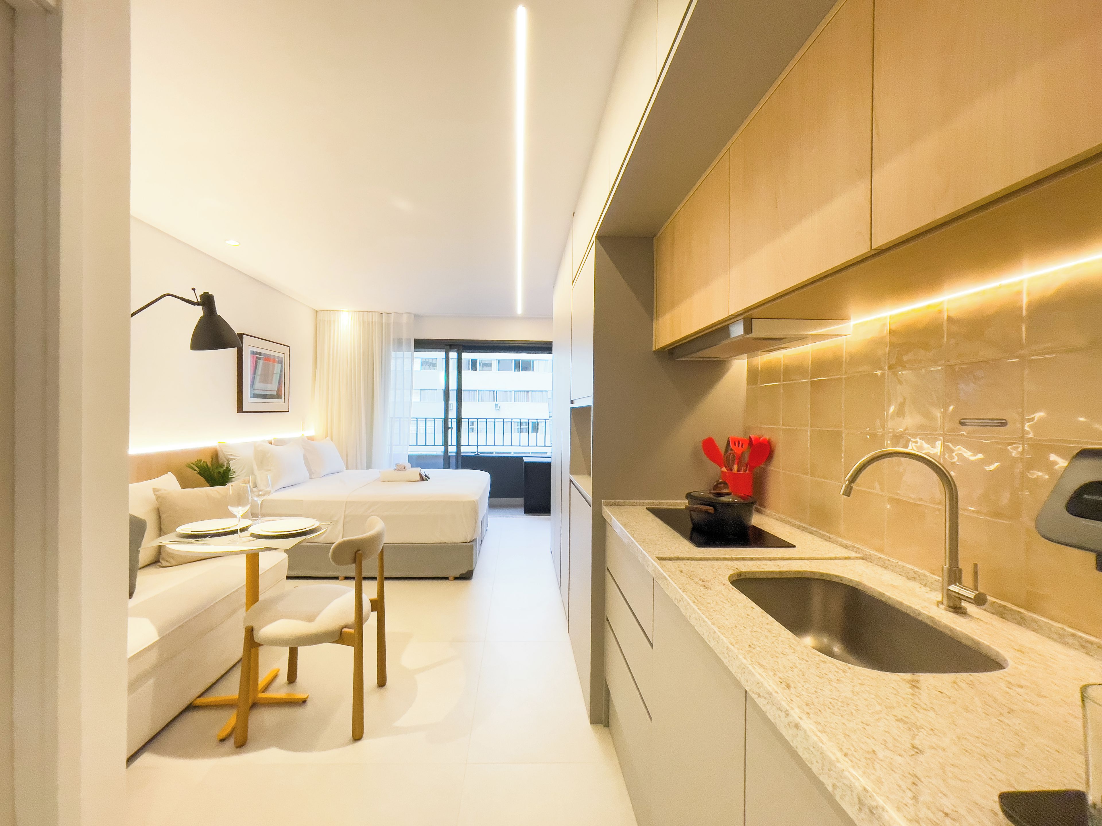 A modern hotel room with a kitchenette, a dining area with a table and chairs, and a bed.