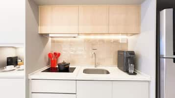 A modern kitchen with white cabinetry, a stainless steel refrigerator, a coffee maker, and a sink.