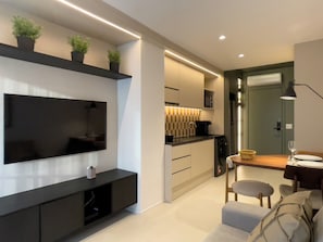 Una sala moderna con televisor de pantalla plana, un mueble de entretenimiento negro, un sofá y una zona de comedor con mesa y sillas.