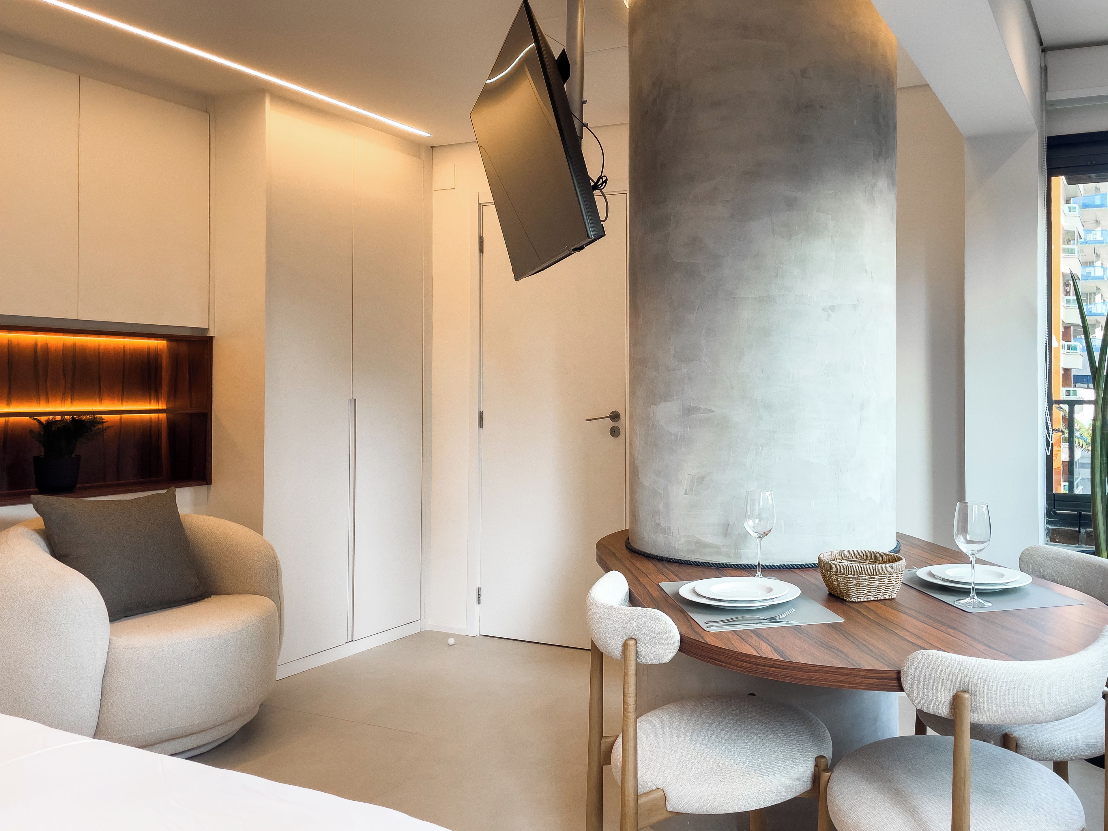 A modern interior with a dining area, a large pillar, and a television mounted on the wall.