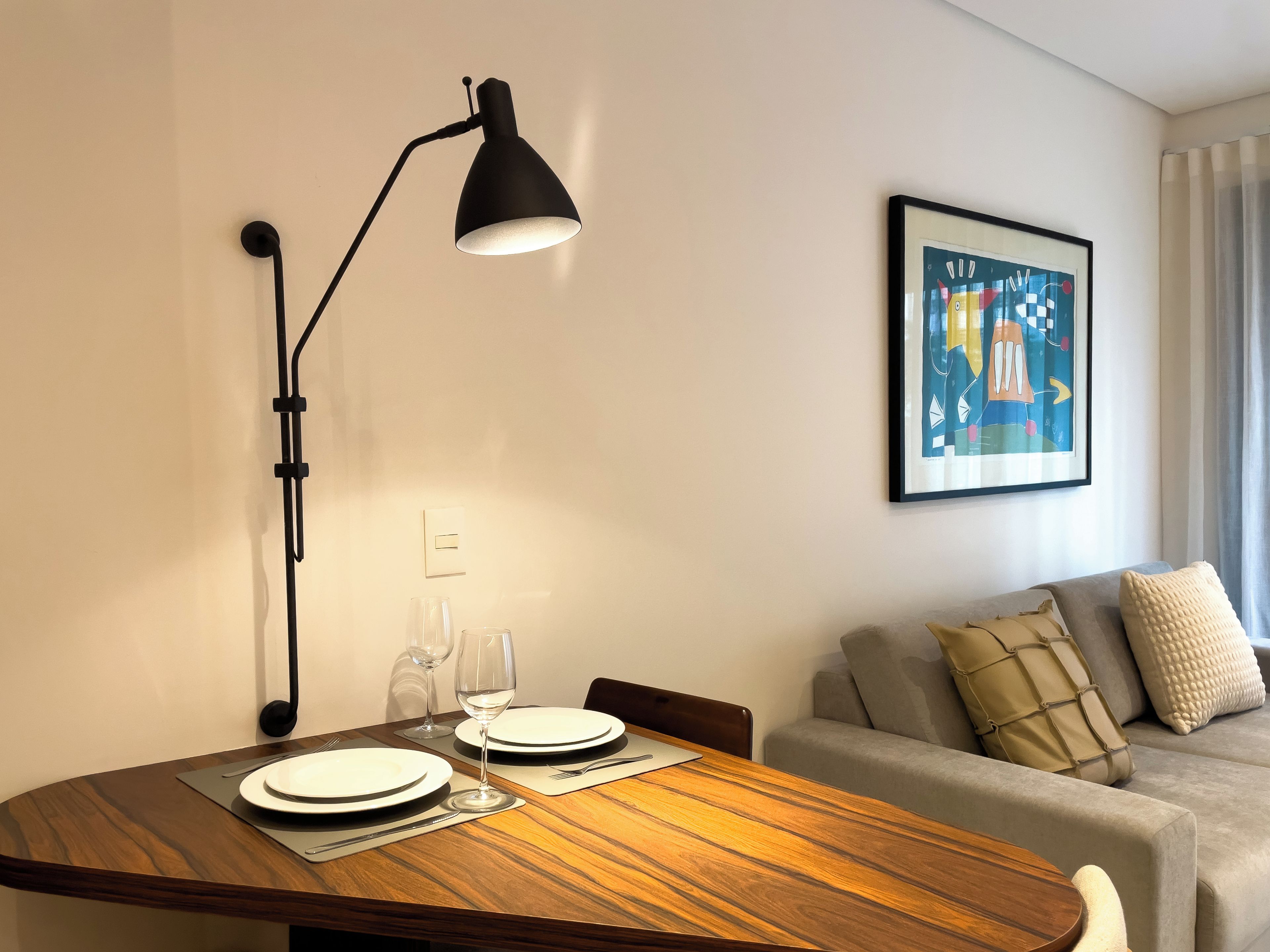 A dining area with a wooden table, two plates, a wine glass, and a black floor lamp.