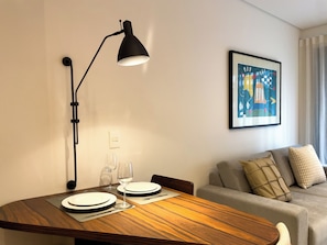 Zona pranzo con tavolo in legno, due piatti, un bicchiere da vino e una lampada da terra nera.