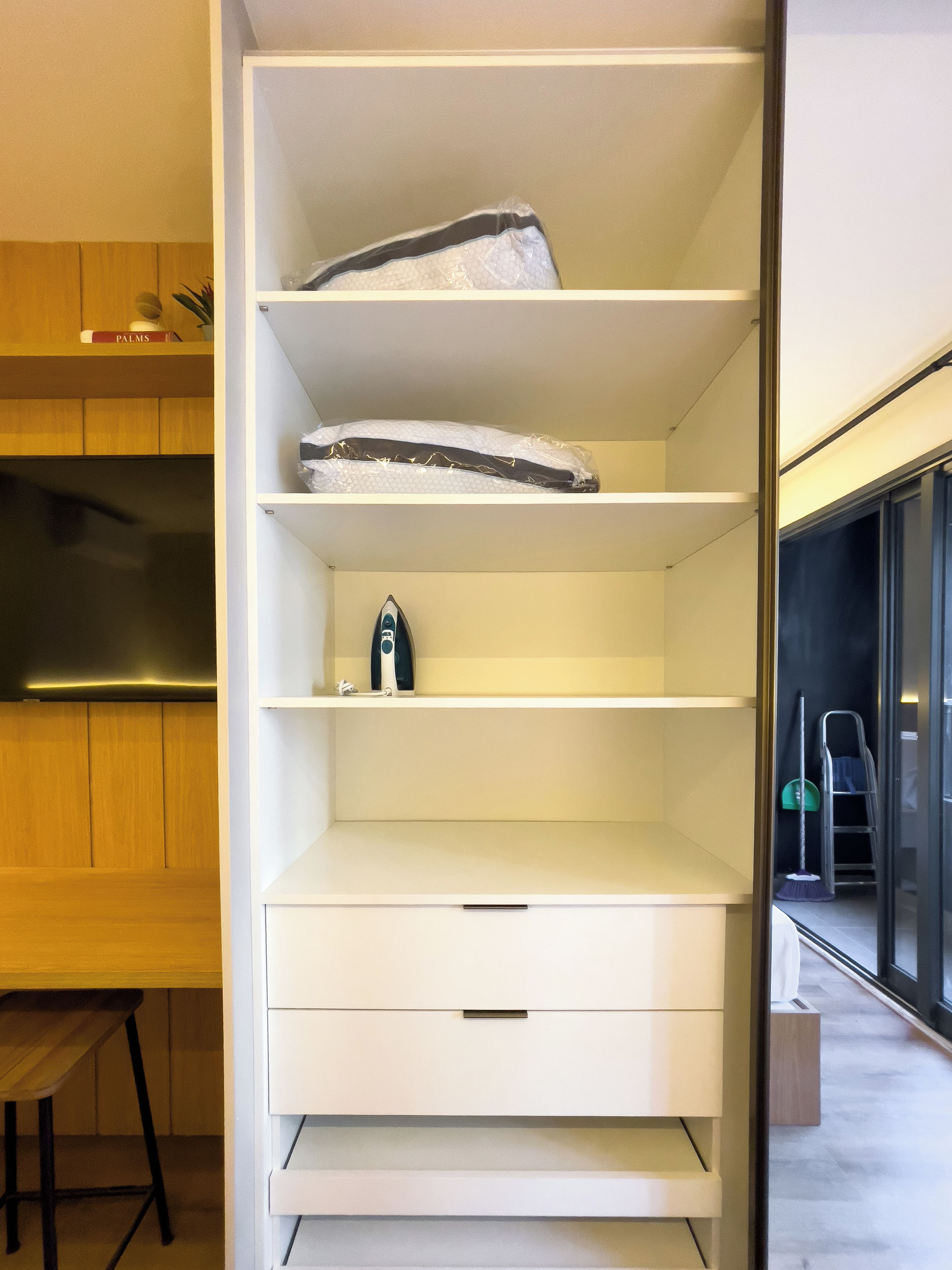 A white storage unit with shelves, a drawer, and a small appliance on the top shelf.