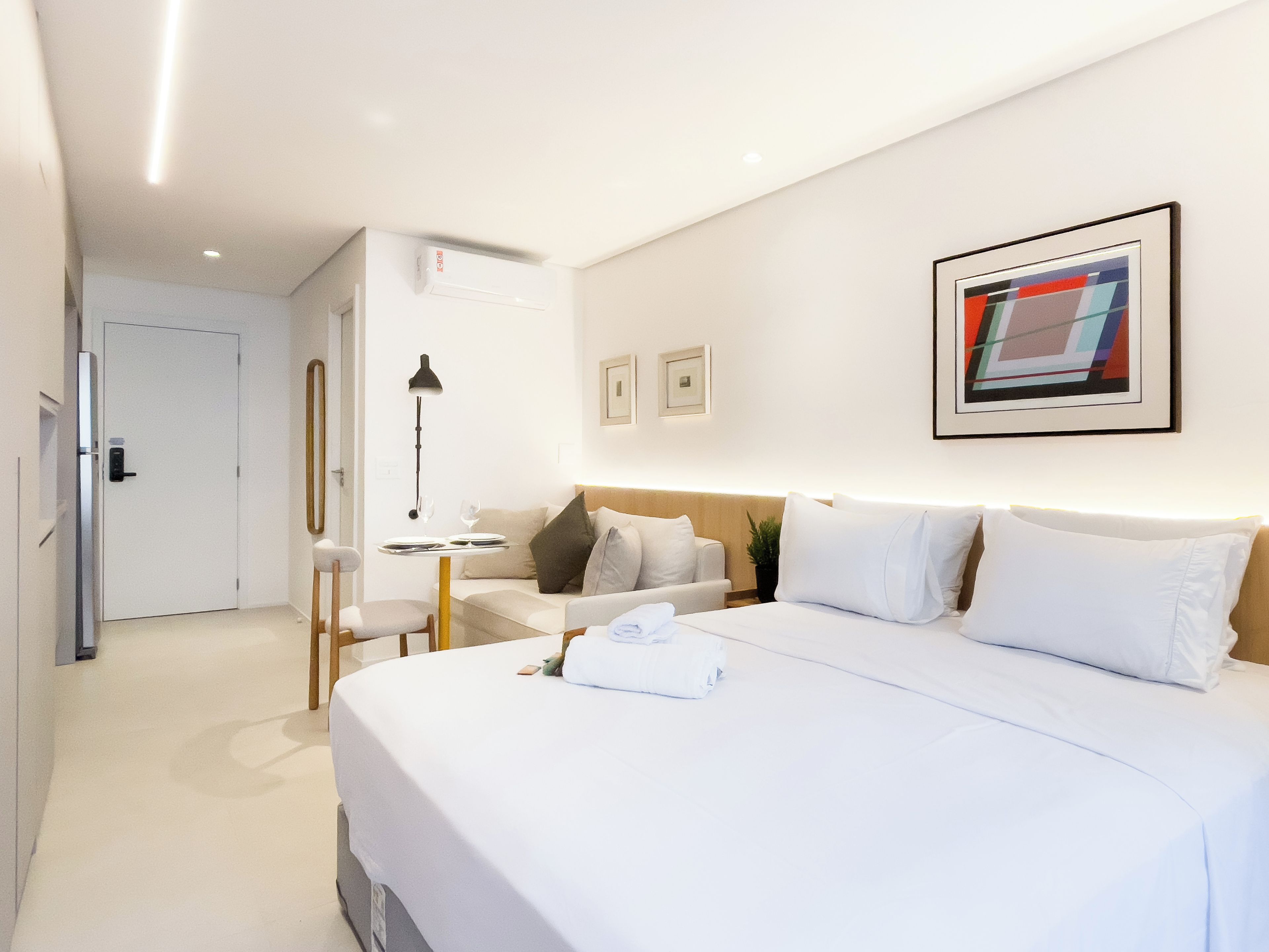 A hotel room with a bed, bedside table, lamp, and a wall-mounted picture.