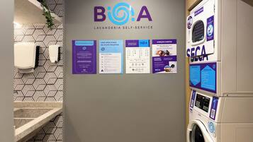 A self-service laundry area with a wall-mounted sign displaying the logo and name 'BioA' along with various instructions and guidelines for use.