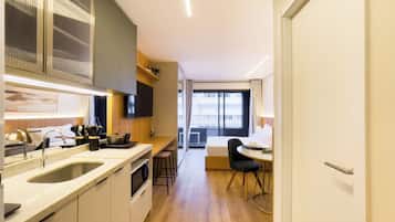 A modern hotel room with a kitchen area, a dining space, and a large window offering a view.