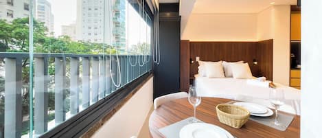 Habitación de hotel con una cama, una mesa de comedor para dos personas y vistas de la ciudad a través de amplias ventanas.