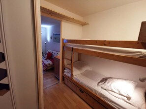 Ein Schlafraum mit Etagenbetten, einem hölzernen Kopfteil, einem kleinen Nachttisch und einer Tür zu einem weiteren Raum.