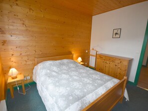 A wooden-paneled room with a bed, bedside lamps, a wooden dresser, and a wall-mounted picture. - Spacious quiet and sunny T4 - 7 guests (Les Gets)