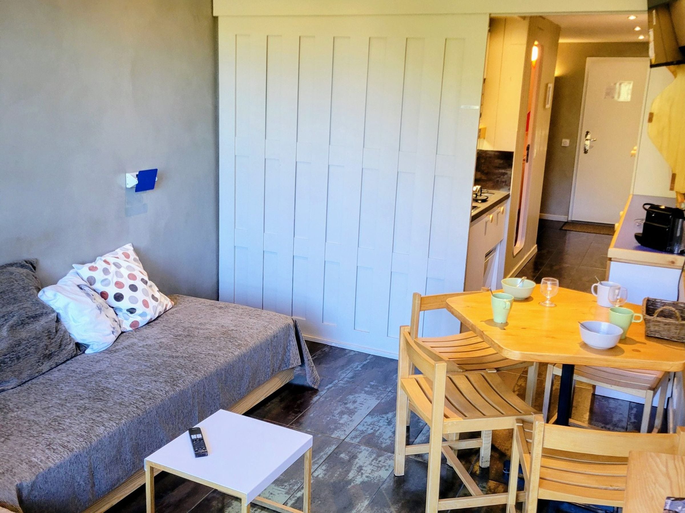 Un espacio habitable compacto con sofá, una mesita y una zona de comedor con sillas.