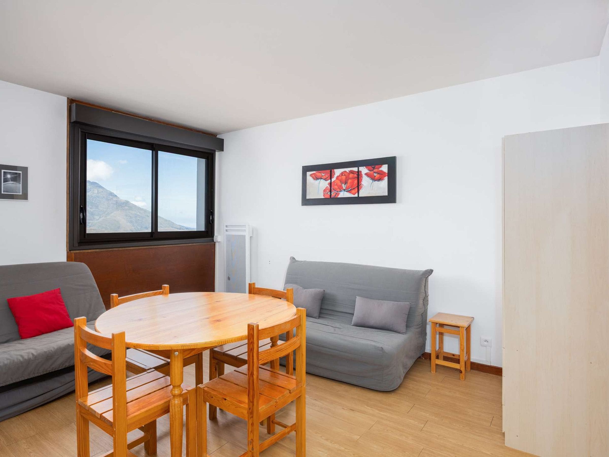 A room with a wooden dining table, grey sofa, and a window with a mountain view.