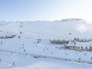 Ein mit Schnee bedeckter Skipisten mit Seilbahn, Berghütte und Berg im Hintergrund.
