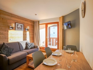 Ein gemütliches Zimmer mit einer Couch, einem Esstisch für zwei Personen und Blick auf eine verschneite Landschaft.