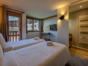 Hotellihuone, jossa on kaksi sänkyä, työpöytä, tuoli, patteri ja ikkuna, josta on näkymä rakennuksiin.