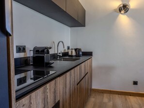 A modern kitchen with a black countertop, wooden cabinets, a built-in coffee machine, a kettle, and a wall-mounted light fixture. - Practical apartment at the ski slopes - 6 guests (Belle Plagne)