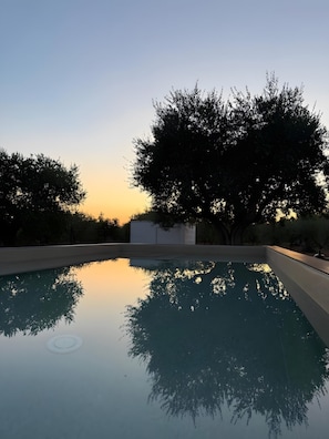 Una piscina con el reflejo nítido de árboles y un edificio al fondo.