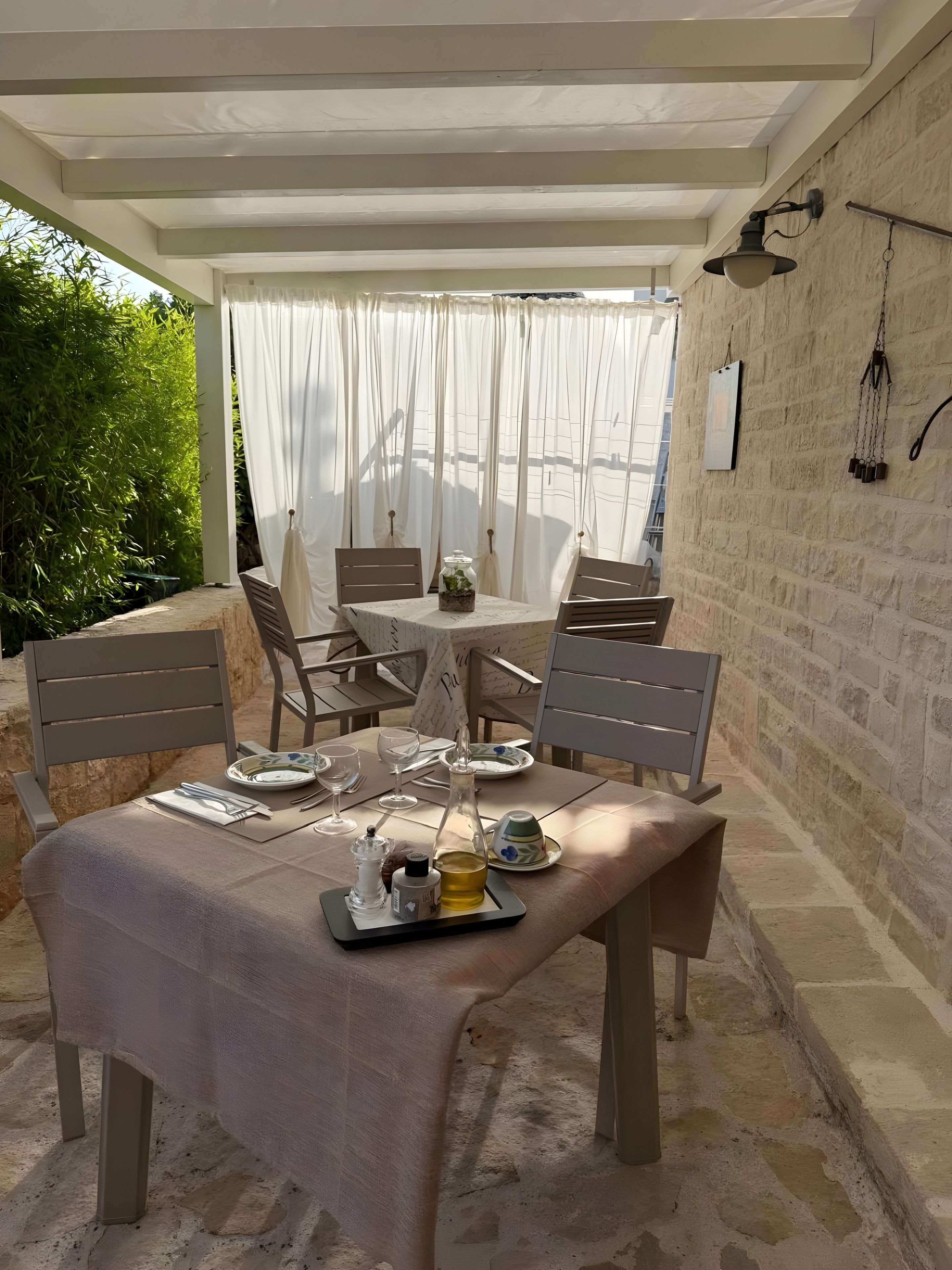 An outdoor dining area with a table set for two, chairs, a glass bottle, and a small plant on the table.