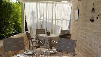 An outdoor dining area with a table set for two, chairs, a glass bottle, and a small plant on the table.