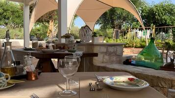 Un espace de restauration en plein air avec une table dressée pour deux personnes, offrant une vue dégagée sur le jardin et les arbres environnants.